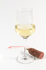 Glas Weisswein und ein Stück Salami auf weißem Hintergrund