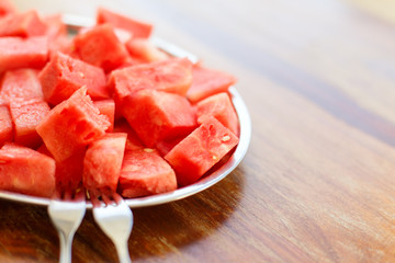 Metal oval dish with a bunch of slices of sliced juicy watermelon with dessert forks on wooden background in sunlight, close up