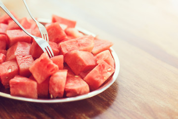 Metal oval dish with a bunch of pieces of sliced juicy watermelon with dessert forks on wooden background in sunlight, close up, toned