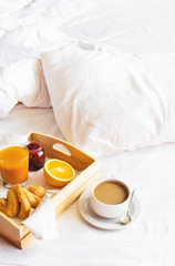 Morning breakfast in bed wooden tray with a cup of coffee croissant orange juice fresh orange jam Bed linen. Top view Hotel Room Early Morning at Hotel Background Concept Interior Copy Space