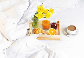 Morning breakfast in bed wooden tray with a cup of coffee croissant orange juice fresh orange jam bouquet of flowers daffodils. Top view Morning at Hotel Background Concept Interior Copy Space