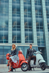 Attractive romantic couple, a handsome man and sexy female, standing with two retro Italian scooters against a skyscraper.