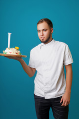 young male confectioner in a tunic with cake in the studio