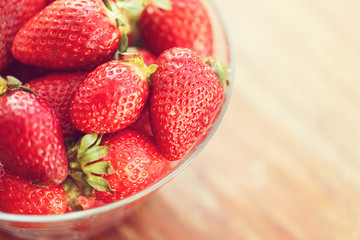 glass bowl with ripe red strawberries on vintage wooden background in sunlight, copy space, closeup