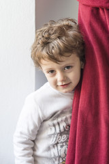 Child hiding behind a red curtain with smiling gesture