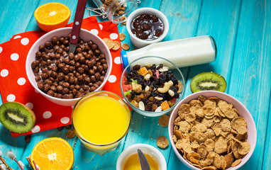 Healthy breakfast with bowl of cereal, orange juice, granola, milk, jam and fruits on blue wood background.