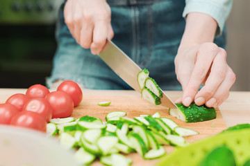 close-up of female hands cut into fresh cut cucumbers on a wooden cutting board next to pink tomatoes. The concept of homemade vegetarian cuisine and healthy eating and lifestyle