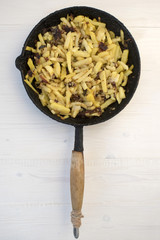 Home fried potatoes in an old frying pan on a light wooden background
