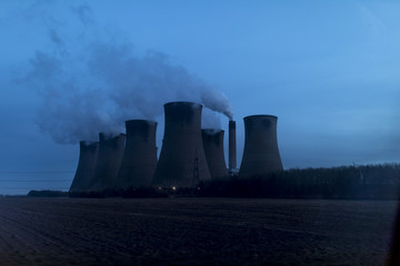Naklejka na ściany i meble Silhouette of a large coal-fired power station in England, United Kingdom, bellows smoke and steam at dusk in the early evening against a deep blue sky