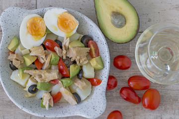 Potaoes, tuna, avocado, hard-boiled egg salad and a white wine glass from above.