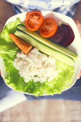 A girl holds a plate with rice and vegetables. Healthy eating concept. Girl in jeans and a plaid shirt. Proper nutrition. Diet. Health. Vegetarian food. Vegans food. Small depth of field. Toned image.