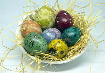 Theme Easter. Multicolored quail eggs on straw in a small bowl.