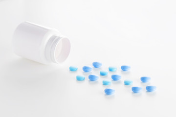 Medical blue pills and white bottle on light white background.