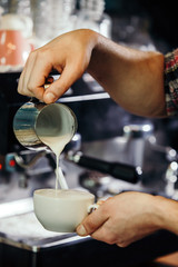 Waiter hands pouring milk making cappuccino