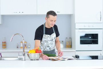 domesticated man in kitchen looking through recipe magazine
