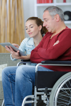 young woman teaching the man on the wheelchair with technology