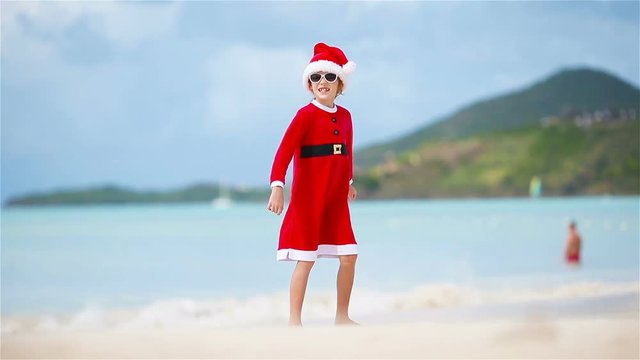 Adorable girl in Christmas hat on white beach during Xmas vacation