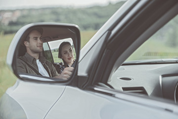 Cute pleasant couple is traveling by car. They are sitting with smile. Focus on mirror with their reflection. Copy space in the right side