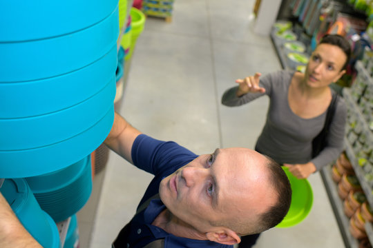 gardening store seller helping female buyer to reach a pot