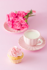 Cupcake with pink cream decoration and roses on pink pastel background.