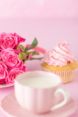 Cupcake with pink cream decoration and roses on pink pastel background.