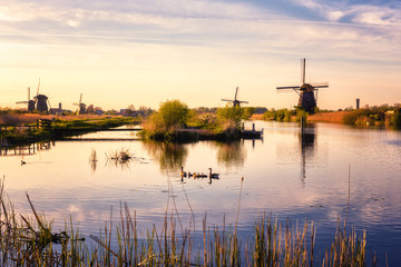 Fototapeta na wymiar Scenic sunset landscape with windmill, blue sky and reflection in the water. Traditional dutch countryside, famous village of mills Kinderdijk, Netherlands (Holland)