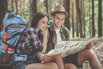 Glad loving couple is sitting and reading a map in forest. Woman is hugging man with smile