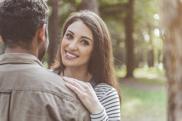 Obraz premium Happy man and woman cuddling in nature. Woman looking at camera with pretty smile. Copy space in right side