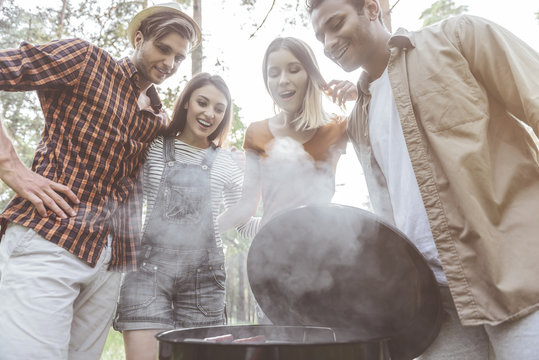 So Delicious. Low Angle Of Four People Standing Over Open Grill And Looking At Food With Eager