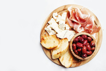 Board with appetizers, crostini, prosciutto, blue cheese and olives, gray background, top view