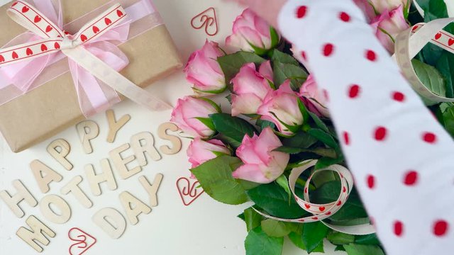 Happy Mother's Day overhead with gift and pink roses on white wood table background.