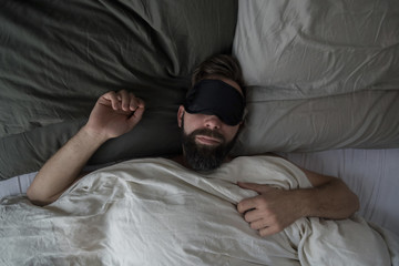 High angle view of man wearing sleep mask while sleeping on bed at home