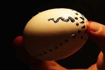 Making of easter egg - half finished tempera colour painted easter egg held in womans hand, dark...