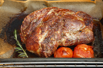 Baked pork meat in the oven. Tomatoes, rosemary, metal baking sheet.