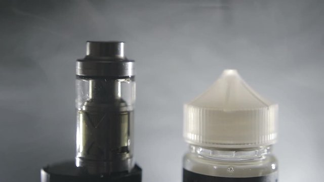 Vape concept. E-cigarette and a jar of liquid for vaping on a background of smoke