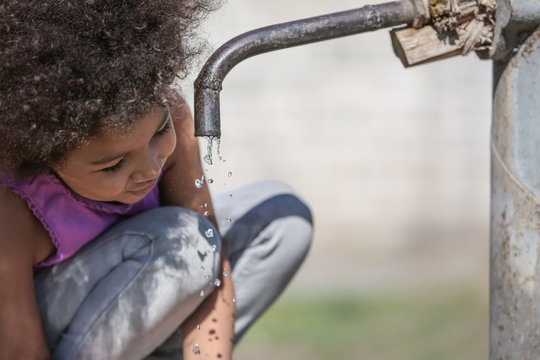 African American child drinking water from tap outdoors. Water scarcity concept