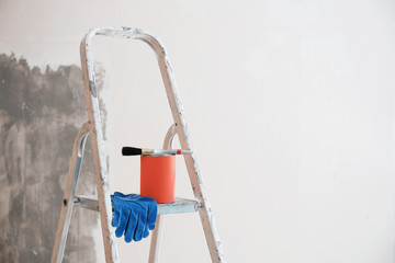 Can with paint and brush on step ladder in room