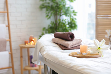 Towels, candles and flower on massage table in spa salon