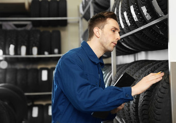 Young male mechanic with clipboard near tires in automobile service center