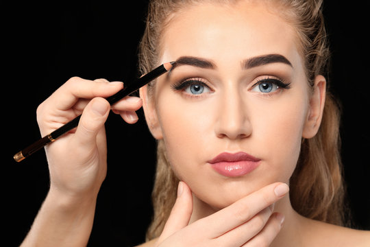 Young woman undergoing eyebrow correction procedure on dark background