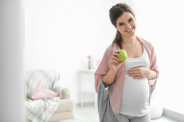 Obraz na płótnie Canvas Young pregnant woman holding apple at home