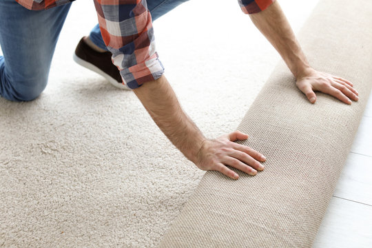 Man Rolling Out New Carpet Flooring In Room