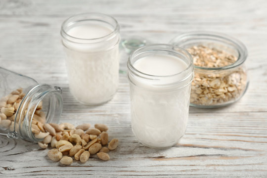Jars with peanut and oat milk on wooden background