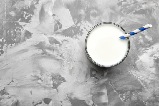 Glass of milk with straw on grey background, top view