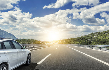 Fototapeta premium Biały samochód pędzący w słońcu szybką autostradą.