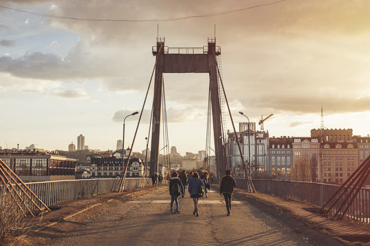 Rear view of friends walking on bridge against cloud during sunset