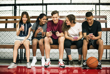 Group of young teenager friends on a basketball court relaxing using smartphone - obrazy, fototapety, plakaty