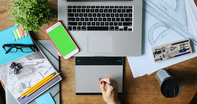 top view of woman hand drawing on digital grapic tablet and smart phone with blank green screen on background art space desk creative business notebook mock-up chroma key designer fashion startup