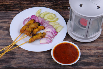 Chicken satay with delicious peanut sauce,  onion and cucumber on wooden  table