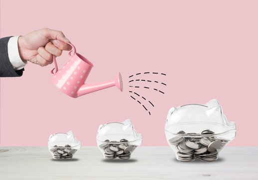 Transparent piggy bank filled with coins on wood background.Saving investment colorful concept.Watering can and money growth drawn concept for business investment, savings and making money.